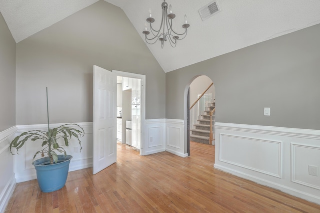 unfurnished room featuring visible vents, light wood-type flooring, vaulted ceiling, an inviting chandelier, and arched walkways