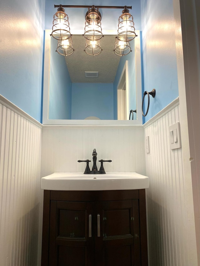 bathroom featuring visible vents, a textured ceiling, a wainscoted wall, and vanity