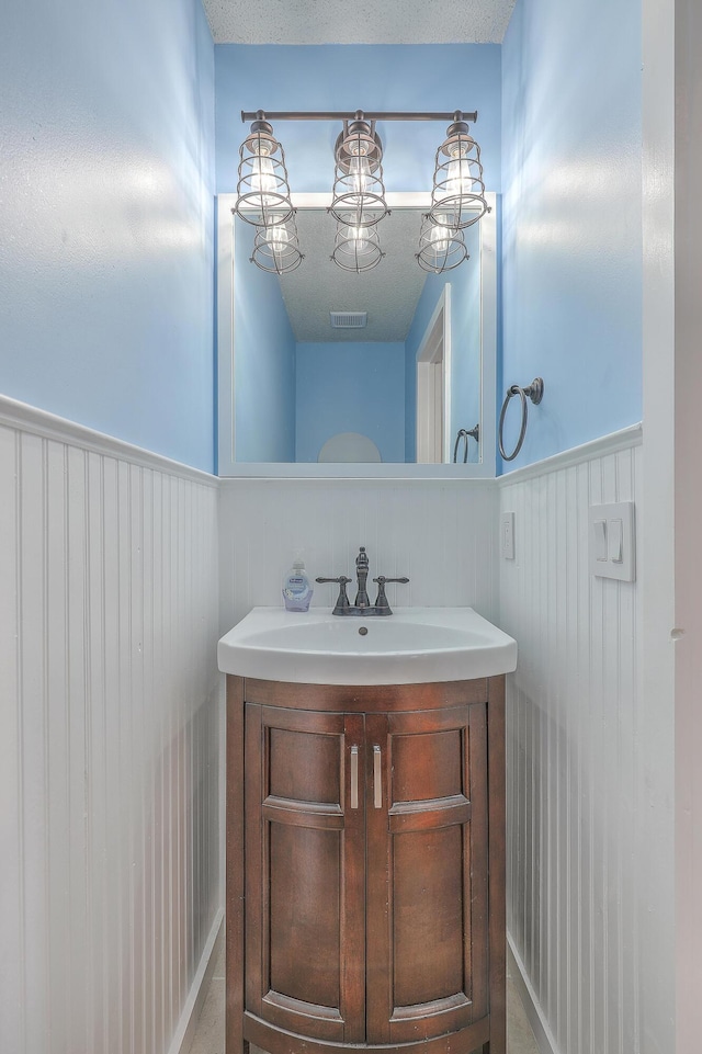 bathroom with visible vents, vanity, wainscoting, and a textured ceiling