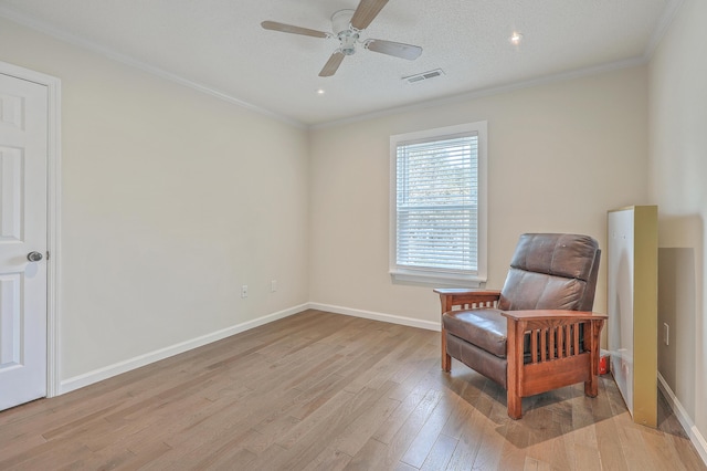 sitting room featuring visible vents, baseboards, ornamental molding, light wood-style floors, and a ceiling fan