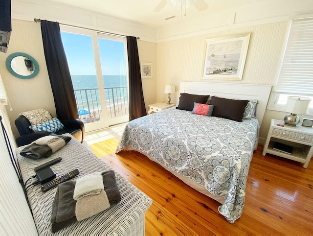 bedroom featuring access to exterior, a water view, wood-type flooring, and multiple windows