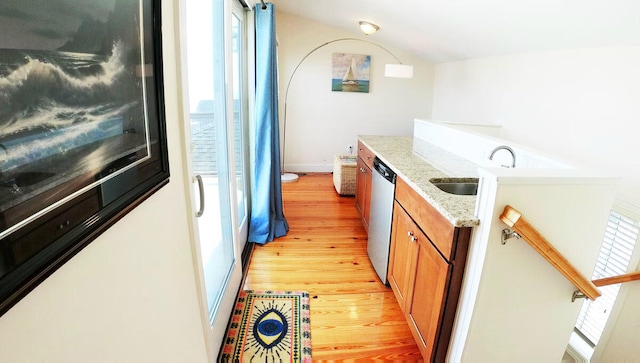 kitchen with light stone countertops, light wood-type flooring, stainless steel dishwasher, and sink