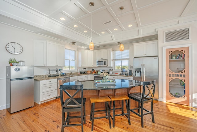 kitchen featuring appliances with stainless steel finishes, coffered ceiling, light hardwood / wood-style flooring, a center island, and white cabinetry