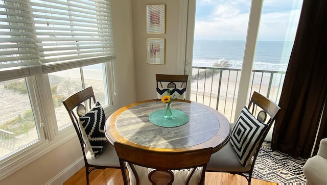 dining area with a water view, a view of the beach, and hardwood / wood-style flooring