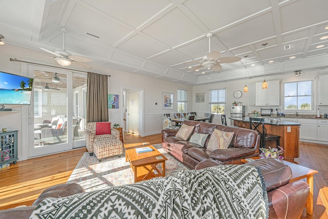 living room featuring light wood-type flooring, plenty of natural light, coffered ceiling, and sink