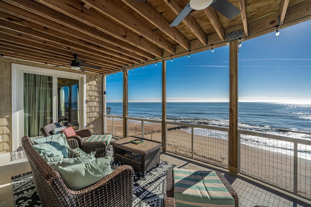 sunroom / solarium featuring ceiling fan, a water view, and a view of the beach