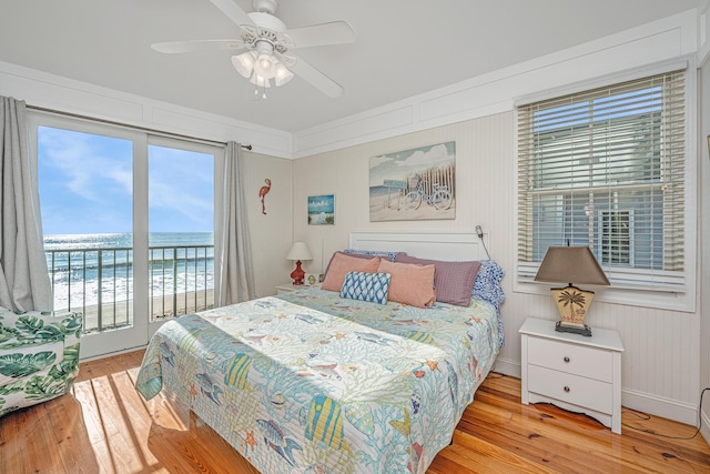 bedroom featuring access to outside, a water view, light hardwood / wood-style flooring, ceiling fan, and a beach view