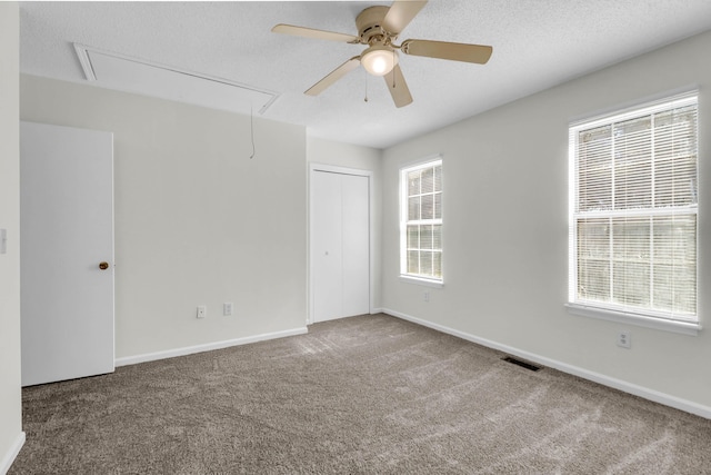 carpeted spare room featuring a textured ceiling, plenty of natural light, attic access, and baseboards