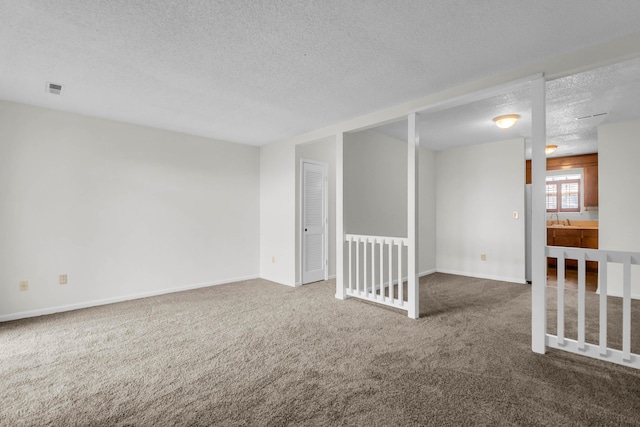 carpeted spare room with visible vents, a sink, a textured ceiling, and baseboards