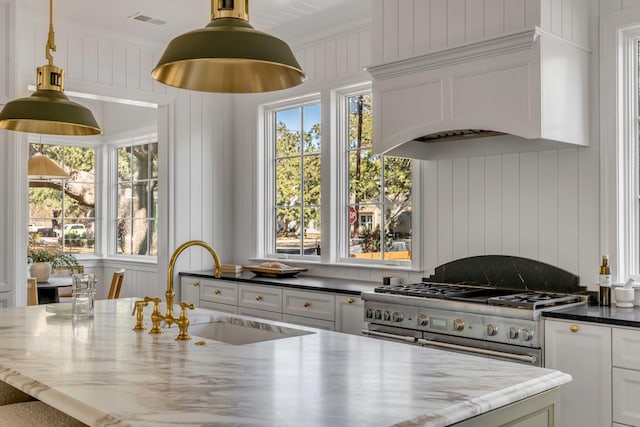 kitchen featuring sink, double oven range, custom range hood, white cabinets, and dark stone counters