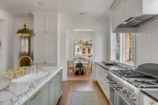 kitchen featuring decorative light fixtures, sink, high end range, dark stone counters, and ornamental molding