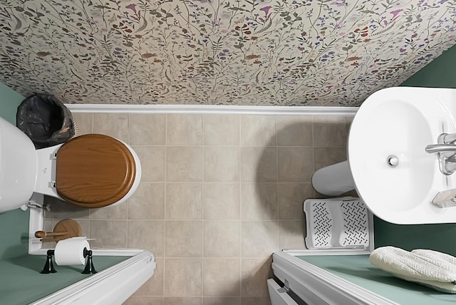 bathroom featuring tile walls, wallpapered walls, a wainscoted wall, and a sink
