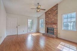 unfurnished living room with a ceiling fan, wood finished floors, a fireplace, baseboards, and vaulted ceiling