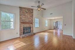 unfurnished living room featuring baseboards, a brick fireplace, wood finished floors, and a ceiling fan