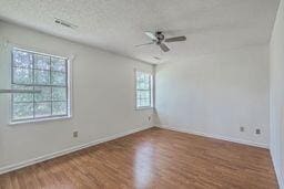 spare room with visible vents, a textured ceiling, wood finished floors, and a ceiling fan