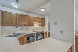 kitchen with light countertops, brown cabinets, range hood, electric range, and a sink