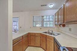 kitchen with a sink, dishwashing machine, brown cabinets, and light countertops