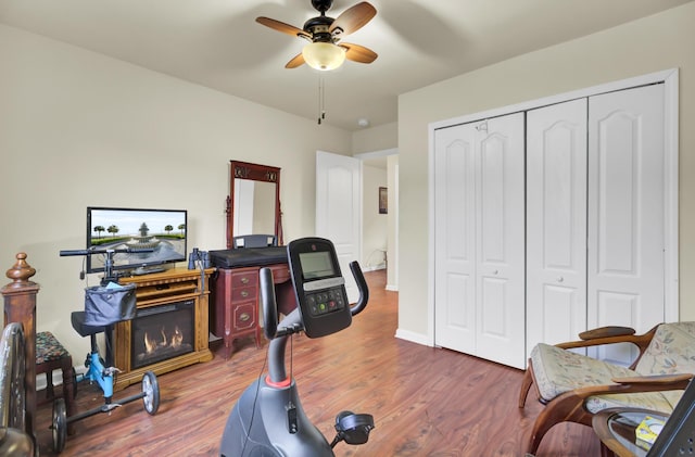 exercise room with wood finished floors, a ceiling fan, and baseboards