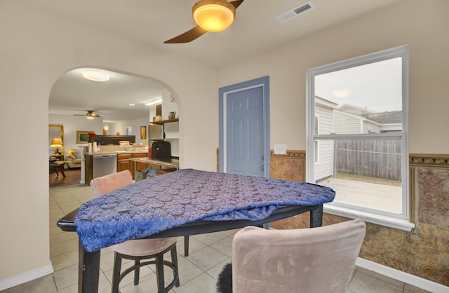 dining room featuring arched walkways, ceiling fan, light tile patterned flooring, visible vents, and wainscoting