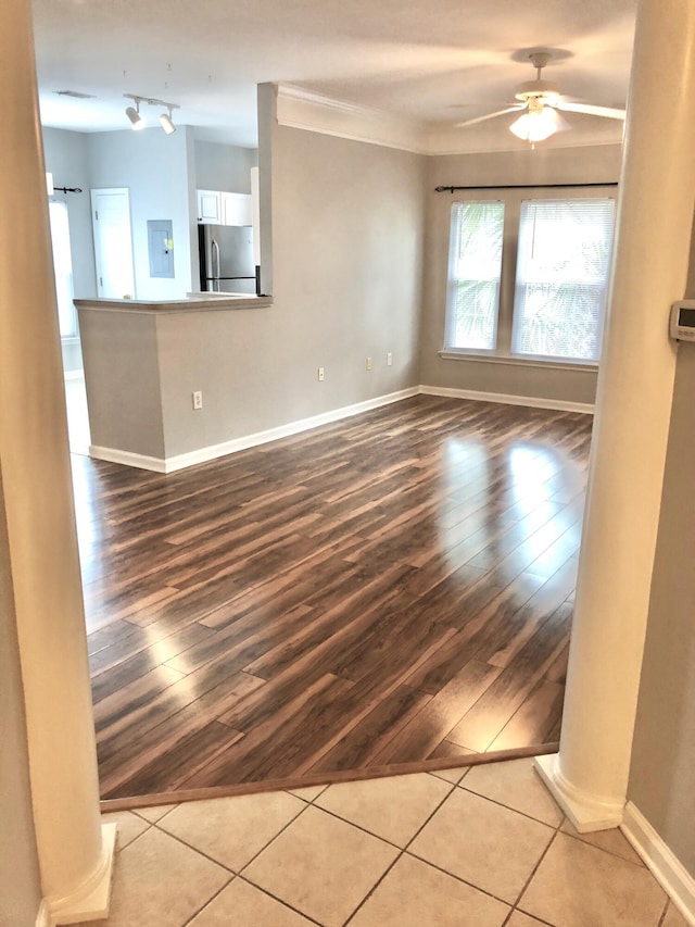 empty room featuring electric panel, crown molding, ceiling fan, light wood-type flooring, and decorative columns