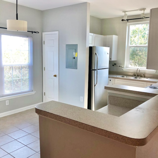 kitchen with stainless steel fridge, sink, electric panel, white cabinetry, and hanging light fixtures