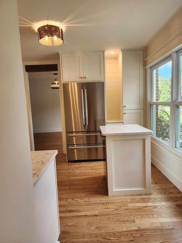 kitchen featuring stainless steel refrigerator, white cabinetry, light stone counters, and light hardwood / wood-style floors