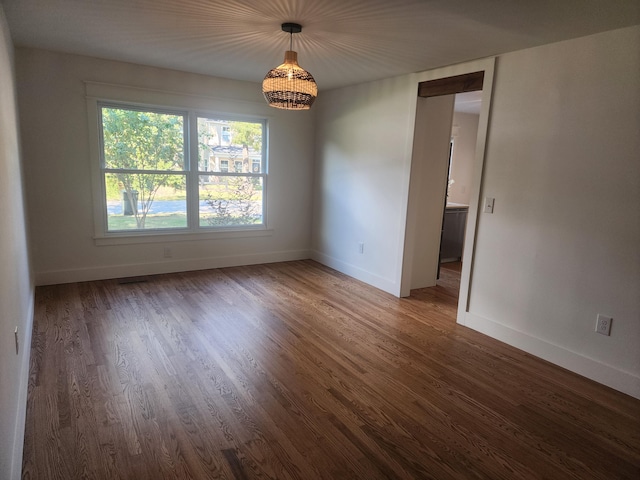 empty room featuring dark wood-type flooring and an inviting chandelier