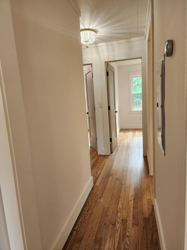 corridor with light hardwood / wood-style flooring, crown molding, and a notable chandelier