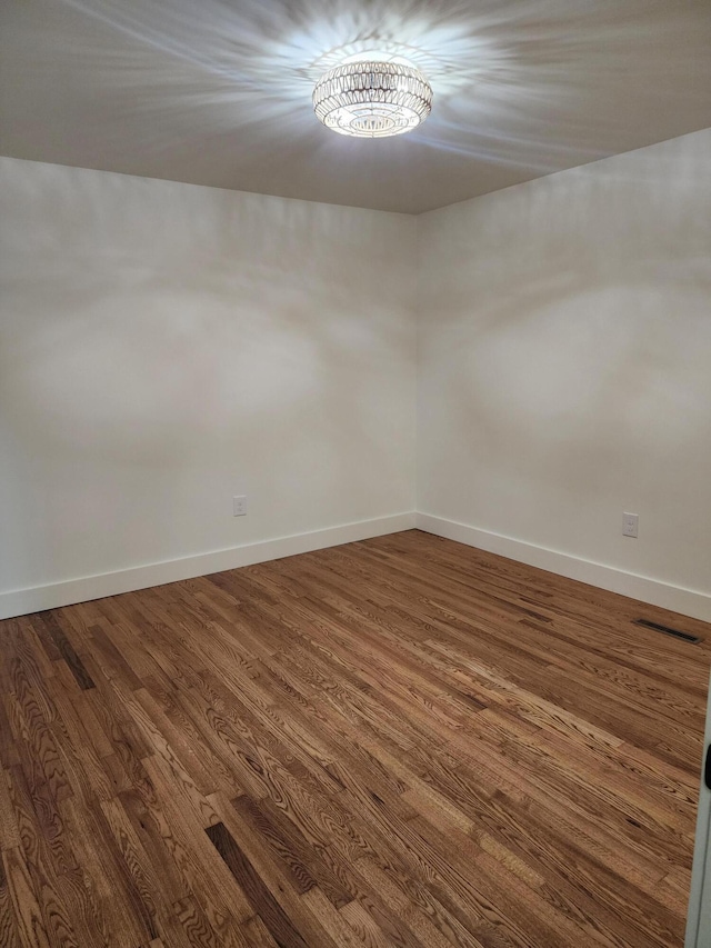 spare room featuring dark wood-type flooring and an inviting chandelier