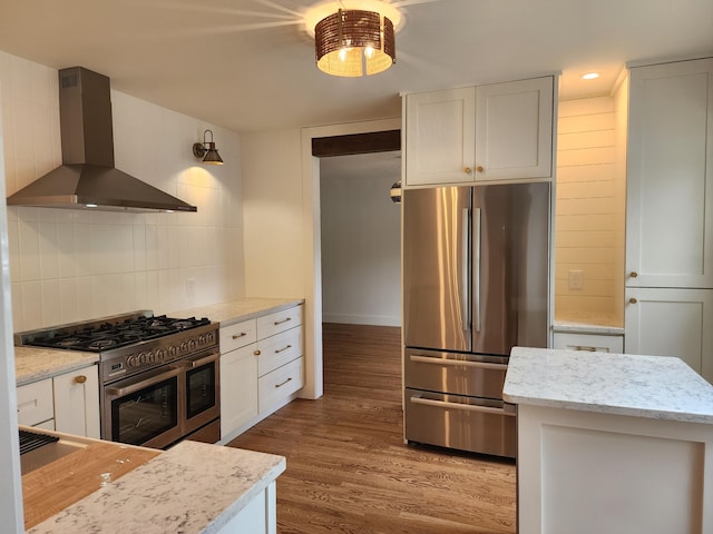 kitchen featuring backsplash, white cabinets, stainless steel appliances, and wall chimney range hood