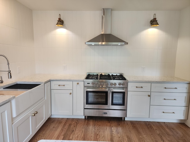 kitchen featuring light stone counters, white cabinetry, double oven range, and wall chimney range hood