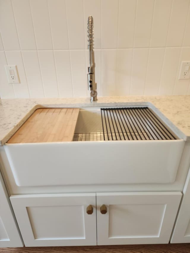 room details featuring white cabinets, light stone countertops, and sink