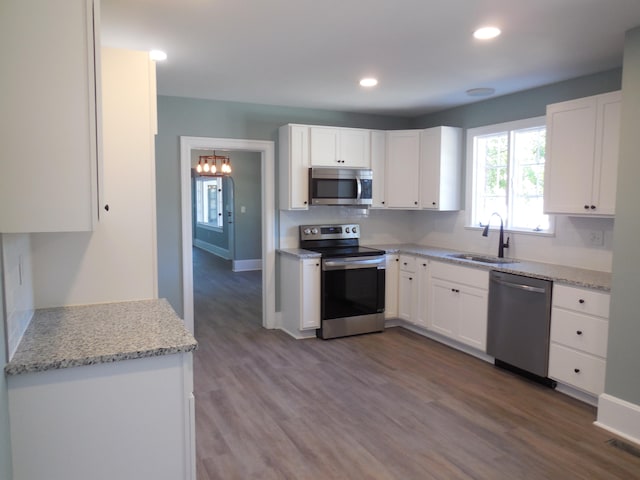 kitchen with white cabinets, light stone countertops, hardwood / wood-style flooring, sink, and stainless steel appliances