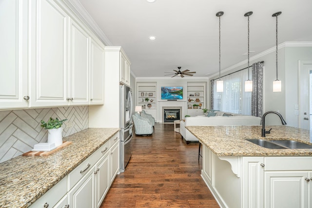 kitchen featuring a sink, open floor plan, ornamental molding, dark wood-style floors, and a glass covered fireplace