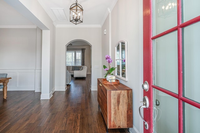 entrance foyer featuring arched walkways, dark wood-type flooring, visible vents, ornamental molding, and an inviting chandelier