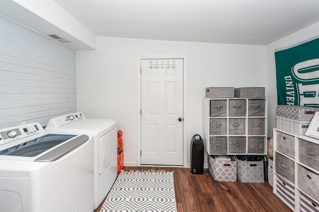 clothes washing area featuring washing machine and dryer, dark hardwood / wood-style flooring, and brick wall