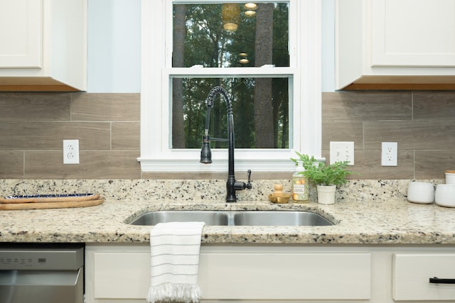 interior details with light stone countertops, dishwasher, tasteful backsplash, sink, and white cabinets