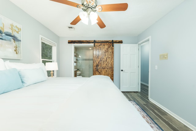 bedroom with a barn door, ceiling fan, ensuite bathroom, and dark wood-type flooring