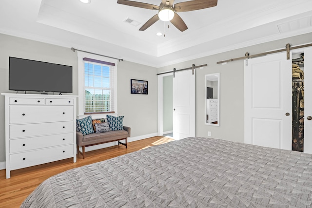 bedroom featuring a barn door, ceiling fan, light hardwood / wood-style flooring, and crown molding