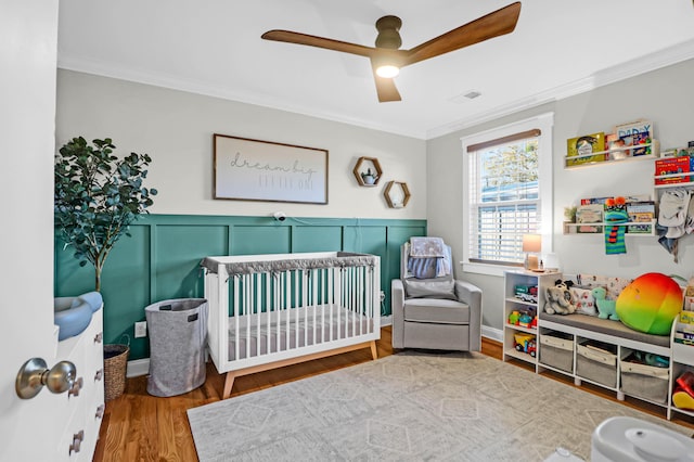 bedroom with ceiling fan, ornamental molding, a nursery area, and hardwood / wood-style flooring