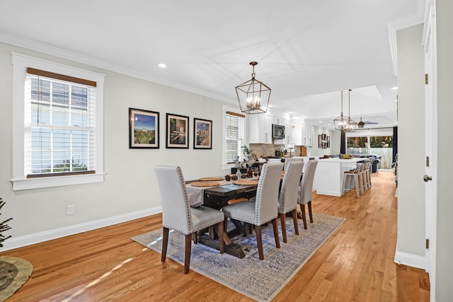 dining room with a healthy amount of sunlight, light wood-type flooring, crown molding, and an inviting chandelier