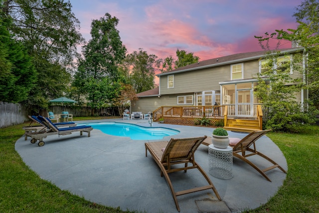 pool at dusk featuring a lawn, a patio area, and a deck