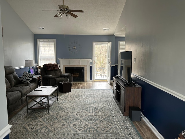 living room with lofted ceiling, a textured ceiling, hardwood / wood-style flooring, ceiling fan, and a tiled fireplace