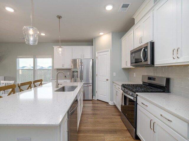 kitchen with hardwood / wood-style floors, a kitchen island with sink, hanging light fixtures, stainless steel appliances, and decorative backsplash