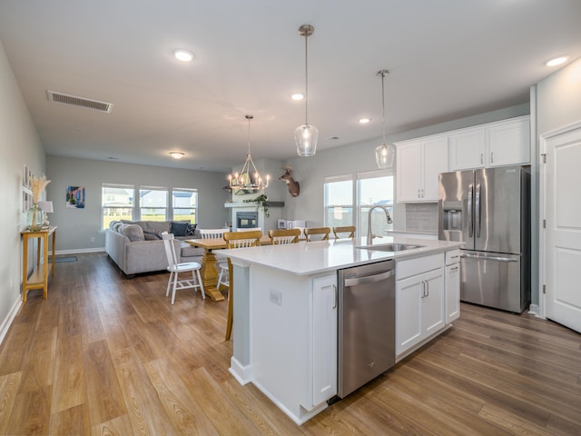 kitchen with stainless steel appliances, an island with sink, white cabinetry, and sink