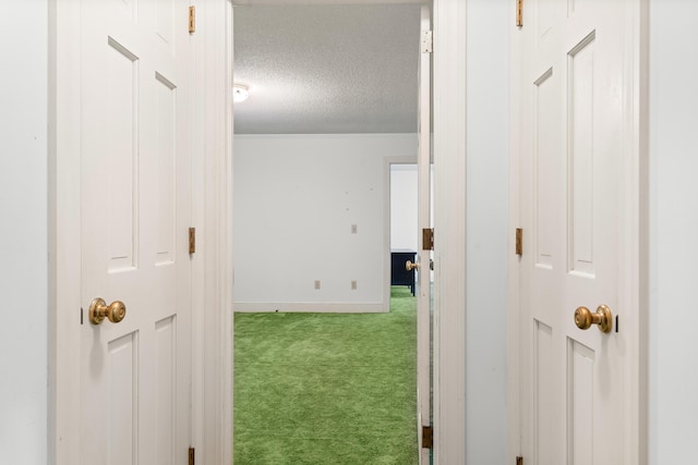 hallway featuring a textured ceiling, carpet flooring, and baseboards