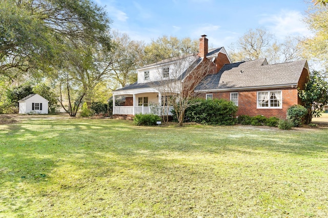 rear view of property featuring a chimney, a yard, covered porch, brick siding, and roof with shingles