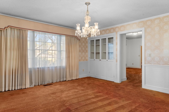 unfurnished dining area with carpet flooring, a chandelier, crown molding, visible vents, and wallpapered walls