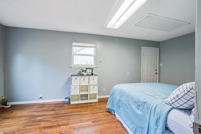 bedroom featuring baseboards, light wood-style flooring, and attic access