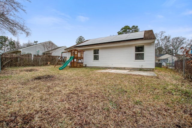 rear view of property with solar panels, a lawn, a playground, and a fenced backyard